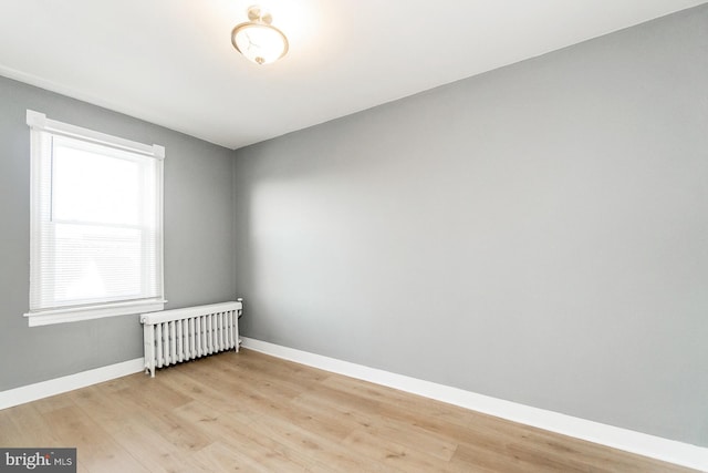 spare room featuring baseboards, light wood finished floors, and radiator heating unit
