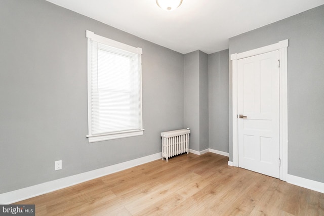 spare room with baseboards, light wood-style flooring, and radiator