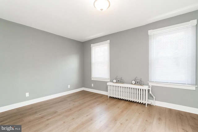 spare room with baseboards, radiator heating unit, and wood finished floors