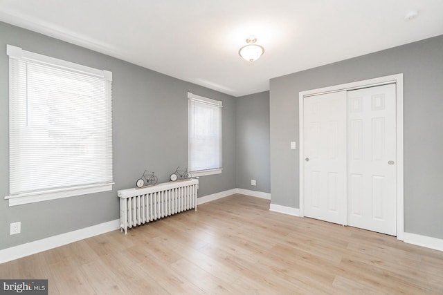 unfurnished bedroom featuring light wood-type flooring, baseboards, radiator heating unit, and a closet
