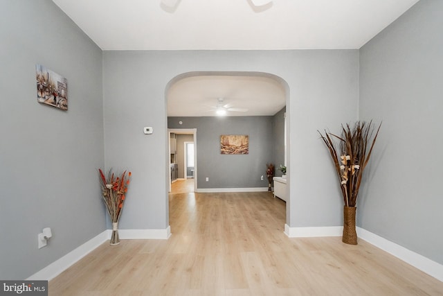 hallway with arched walkways, baseboards, and light wood-type flooring