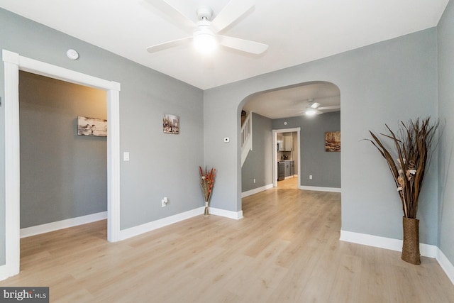 unfurnished room featuring arched walkways, ceiling fan, baseboards, and light wood-type flooring