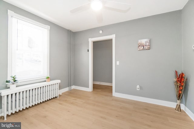 spare room with radiator heating unit, baseboards, a ceiling fan, and light wood finished floors