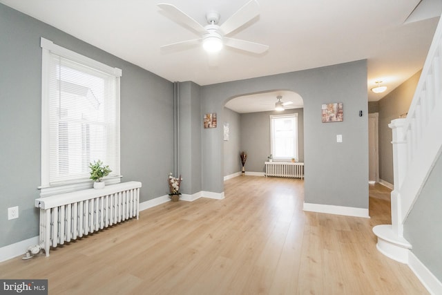 spare room featuring light wood-style floors, arched walkways, ceiling fan, and radiator heating unit
