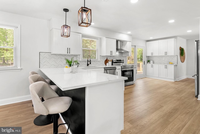 kitchen with a peninsula, a kitchen breakfast bar, wall chimney exhaust hood, a sink, and stainless steel appliances