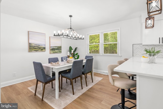 dining space with baseboards, light wood finished floors, visible vents, and an inviting chandelier