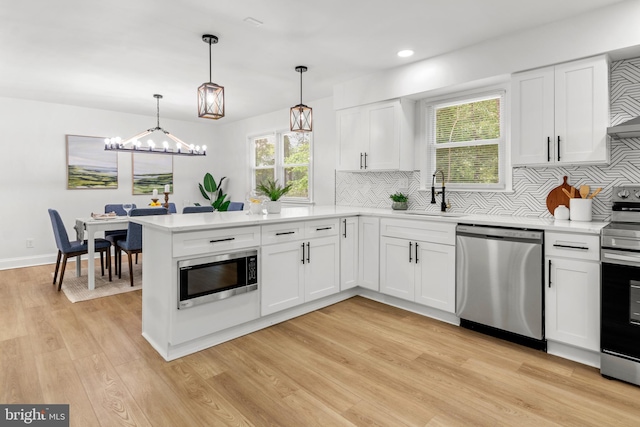 kitchen featuring a sink, light countertops, stainless steel appliances, a peninsula, and backsplash