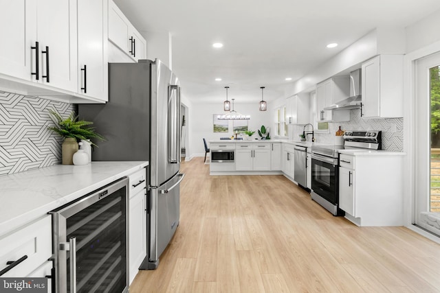 kitchen with appliances with stainless steel finishes, light wood-style flooring, wall chimney exhaust hood, wine cooler, and backsplash