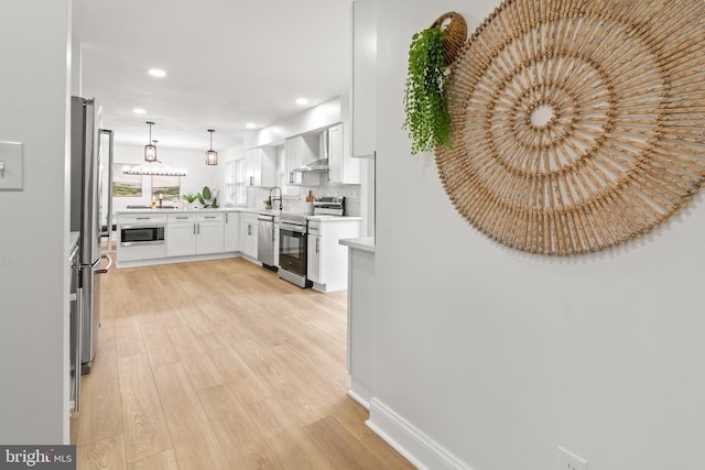 kitchen featuring appliances with stainless steel finishes, light countertops, light wood-style flooring, wall chimney exhaust hood, and recessed lighting