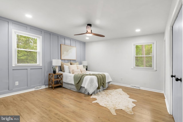 bedroom featuring multiple windows, a decorative wall, light wood-style flooring, and visible vents