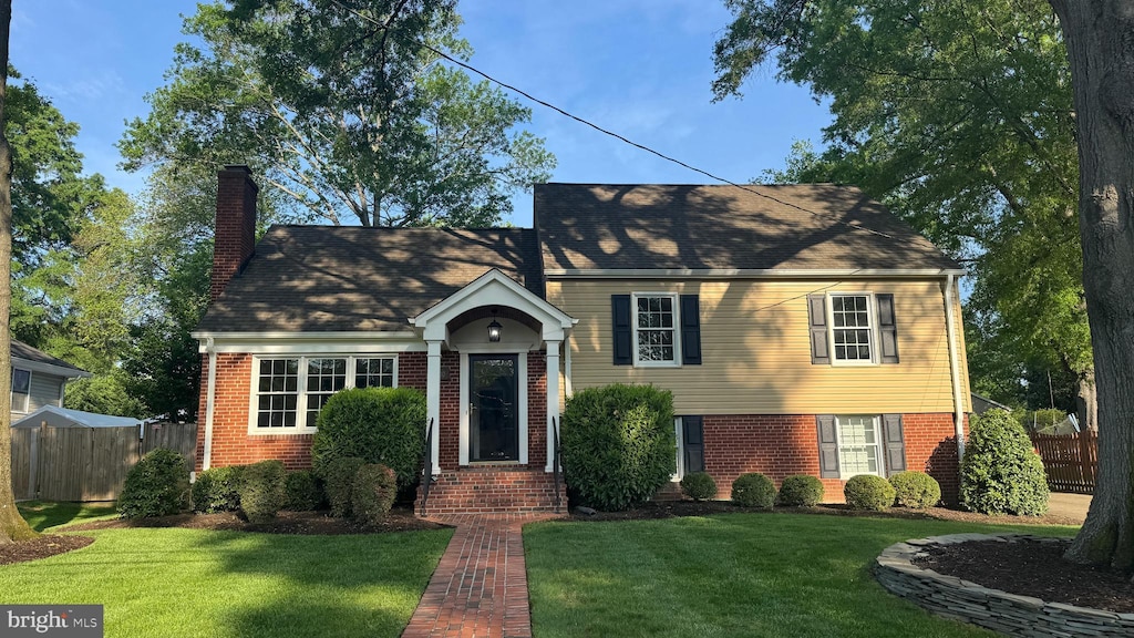 traditional-style house with brick siding, a chimney, fence, and a front yard