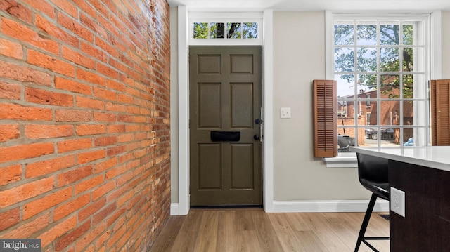 entrance foyer featuring baseboards, a wealth of natural light, brick wall, and wood finished floors