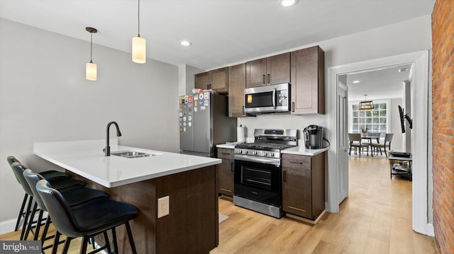 kitchen featuring dark brown cabinetry, a sink, light wood finished floors, a kitchen breakfast bar, and stainless steel appliances