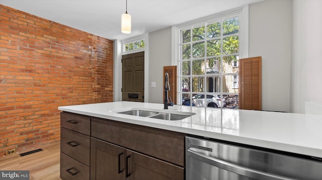 kitchen featuring light countertops, brick wall, a sink, and dishwasher