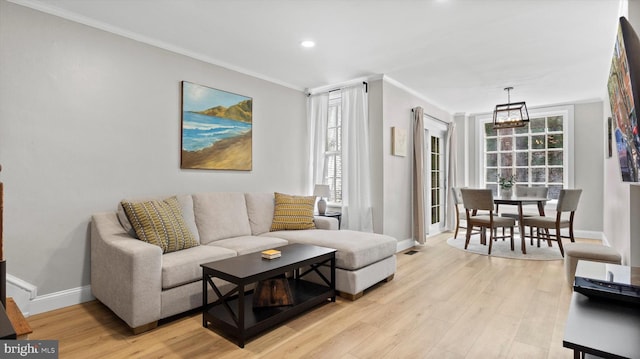 living area featuring crown molding, light wood-style flooring, baseboards, and a notable chandelier