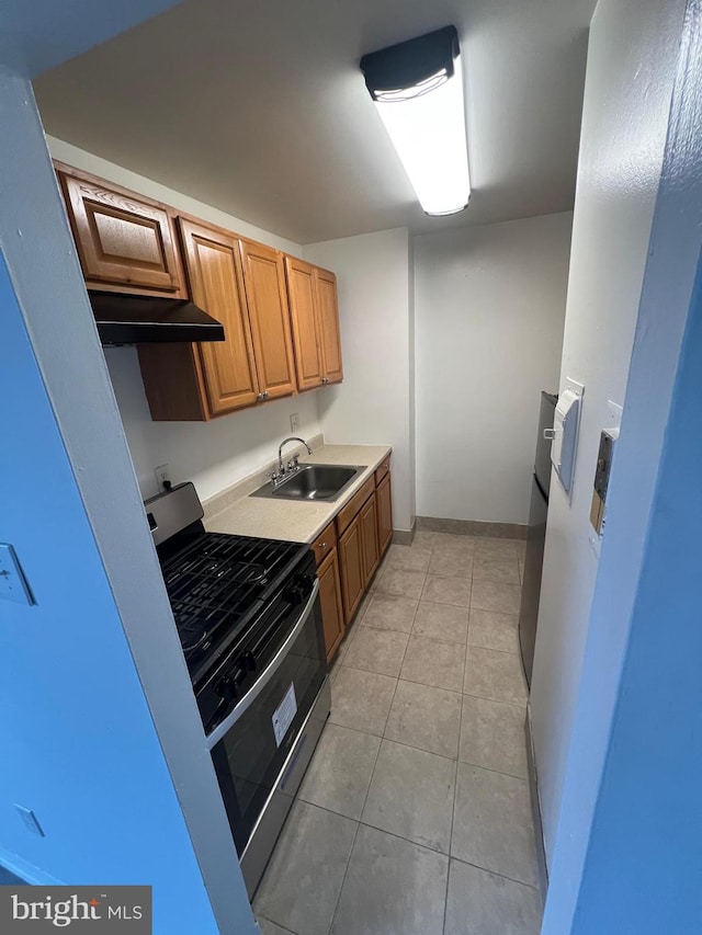 7521 Riverdale Rd Unit 1979, New Carrollton, MD 20784 - kitchen featuring stainless steel gas range, a sink, brown cabinetry, light tile patterned floors, and under cabinet range hood