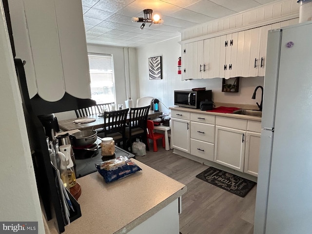 kitchen featuring freestanding refrigerator, wood finished floors, white cabinetry, stainless steel microwave, and a sink
