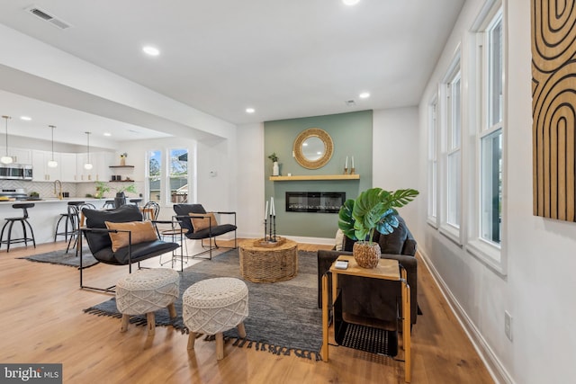living area with visible vents, a glass covered fireplace, baseboards, recessed lighting, and light wood-type flooring