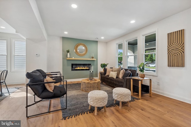 living area featuring baseboards, recessed lighting, a glass covered fireplace, and wood finished floors