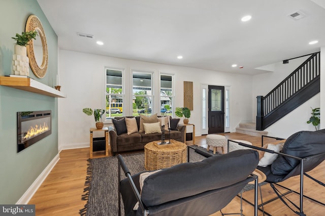 living area with light wood finished floors, a glass covered fireplace, recessed lighting, visible vents, and stairway