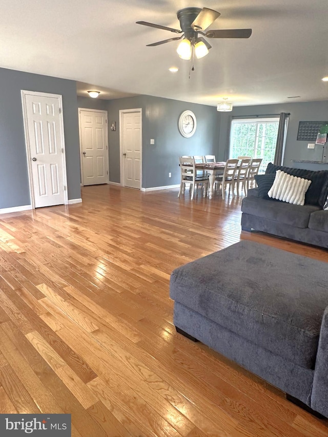 living room with a ceiling fan, light wood finished floors, and baseboards