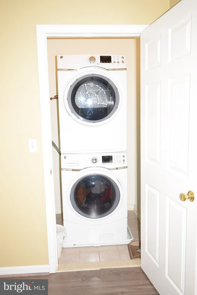 clothes washing area featuring stacked washer / drying machine, baseboards, and wood finished floors