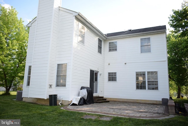 rear view of house with a chimney, a patio, entry steps, a lawn, and cooling unit