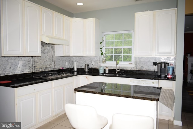kitchen featuring a sink, stainless steel gas stovetop, tasteful backsplash, light tile patterned floors, and under cabinet range hood