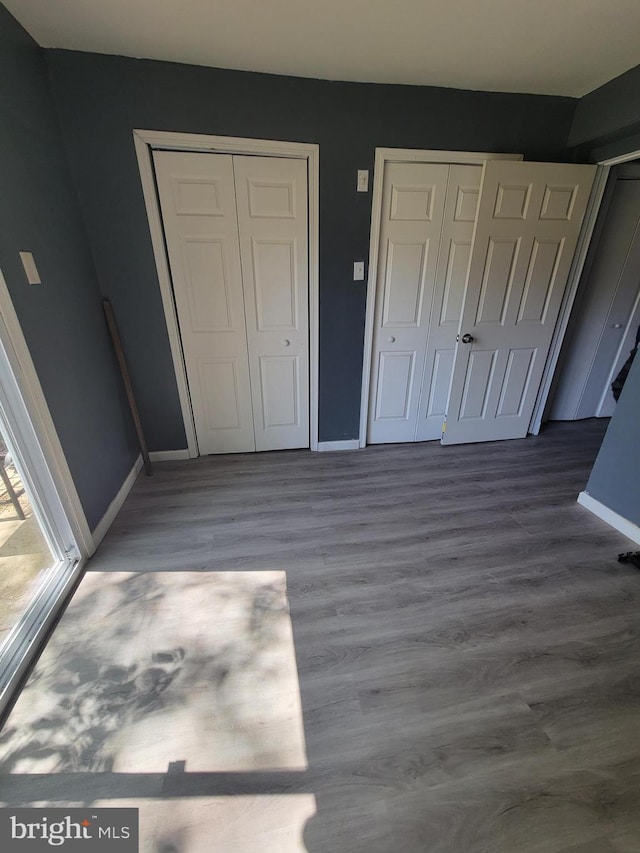 unfurnished bedroom with two closets, baseboards, and wood finished floors