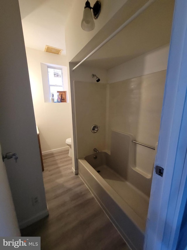 bathroom featuring visible vents, shower / tub combination, wood finished floors, baseboards, and toilet