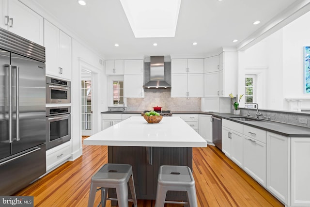 3101 Highland Pl NW, Washington, DC 20008 - kitchen featuring wall chimney range hood, appliances with stainless steel finishes, a sink, a breakfast bar area, and light wood-style flooring