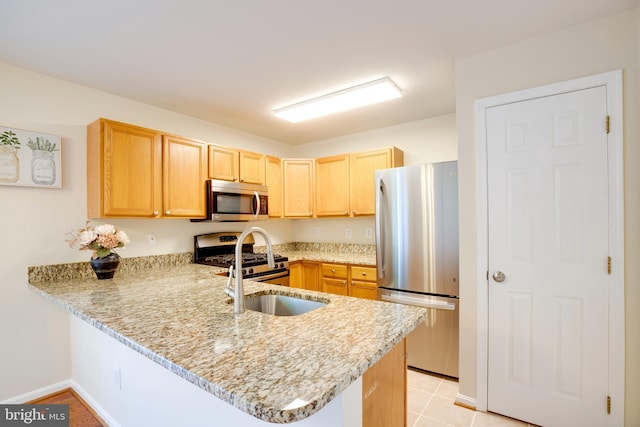 kitchen featuring appliances with stainless steel finishes, a peninsula, light brown cabinetry, a sink, and light stone counters