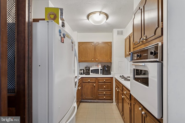 kitchen featuring white appliances, light countertops, brown cabinets, and a textured ceiling