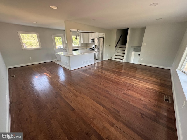 unfurnished living room featuring baseboards, visible vents, dark wood-style flooring, and stairs