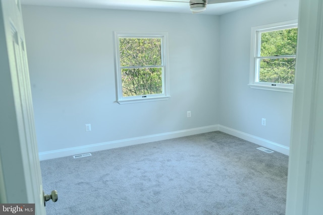 carpeted empty room featuring a healthy amount of sunlight, ceiling fan, and visible vents