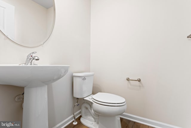 half bath featuring baseboards, toilet, and wood finished floors