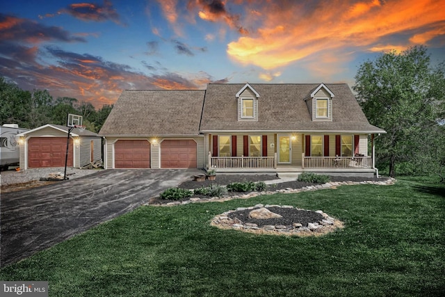 new england style home featuring a porch, a garage, driveway, and a front yard