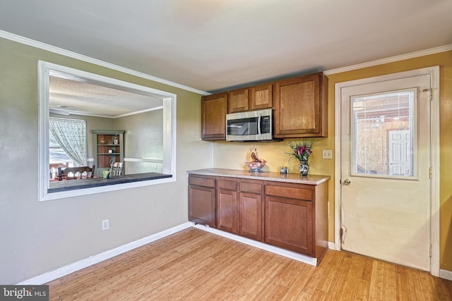 kitchen featuring brown cabinets, light wood finished floors, stainless steel microwave, baseboards, and ornamental molding