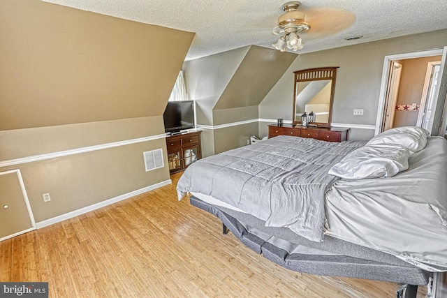 bedroom with visible vents, baseboards, a textured ceiling, and wood finished floors