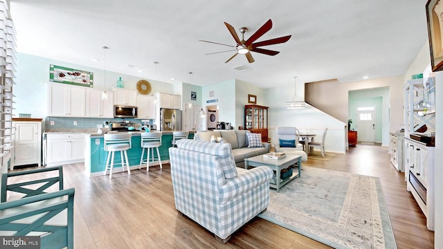 living room with light wood-type flooring, a ceiling fan, visible vents, and recessed lighting