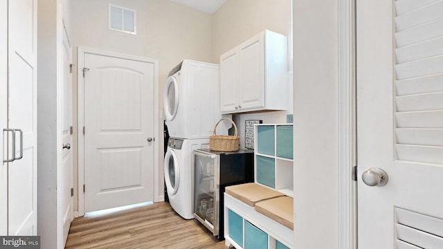 laundry area with stacked washer and dryer, light wood finished floors, visible vents, and cabinet space