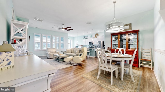 dining space with light wood-type flooring, visible vents, and ceiling fan with notable chandelier