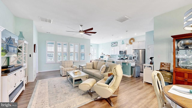living room with baseboards, visible vents, light wood-style flooring, and a ceiling fan
