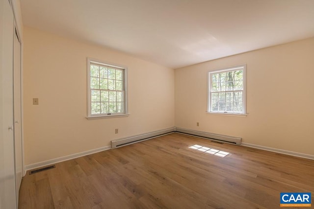 spare room with baseboards, visible vents, wood finished floors, and a baseboard radiator