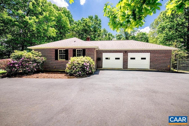 ranch-style home featuring a chimney, brick siding, aphalt driveway, an attached garage, and roof with shingles
