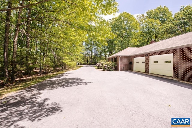 view of property exterior with a garage, a chimney, brick siding, and driveway