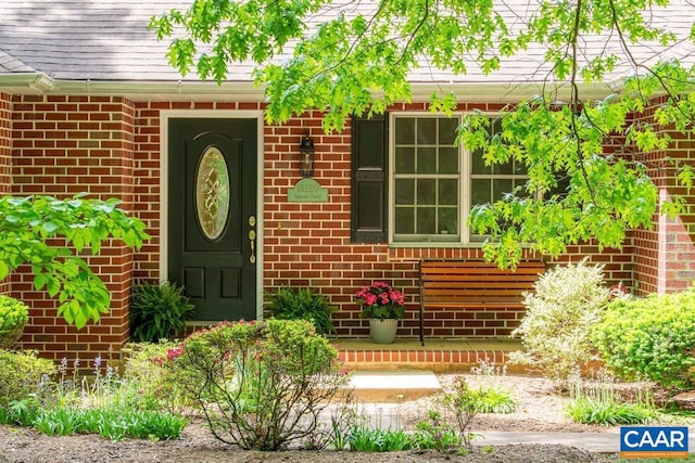 property entrance featuring roof with shingles and brick siding