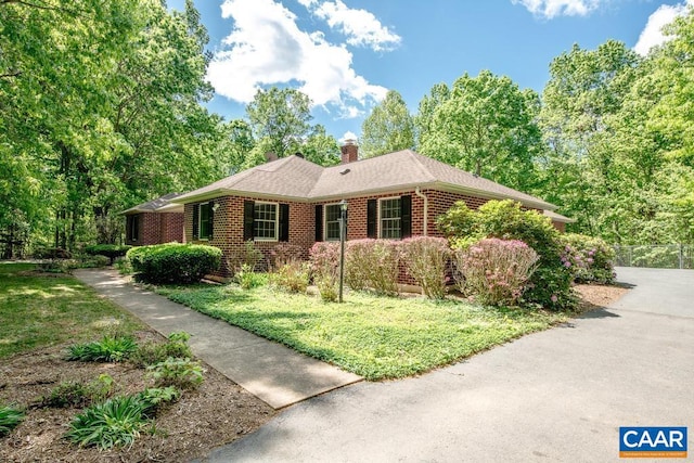 view of side of home with fence, a chimney, brick siding, and a lawn