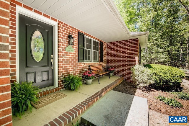 view of exterior entry featuring covered porch and brick siding