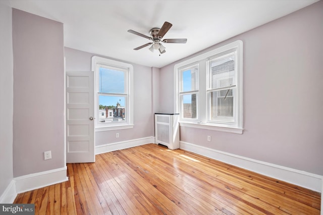 unfurnished room featuring baseboards, ceiling fan, radiator, and light wood-type flooring